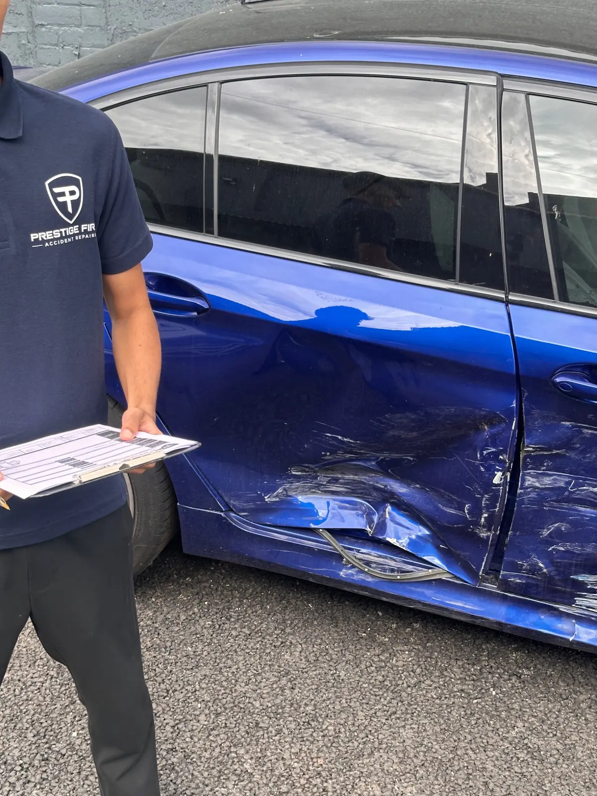 Prestige First team member assessing damage to a blue car door for repair